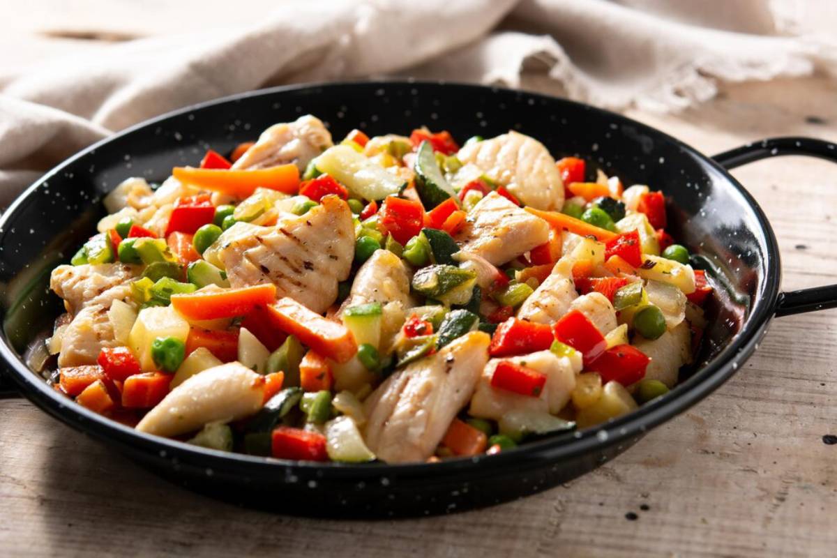 Stir-fried chicken and mixed vegetables in a black skillet on a wooden table.