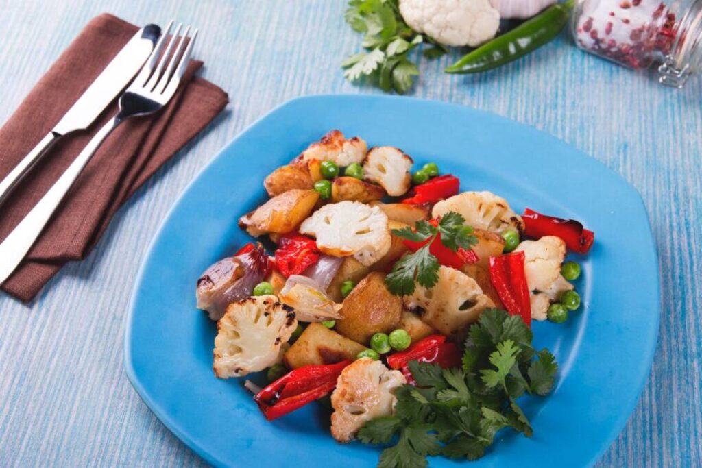 A colourful stir-fried vegetable dish on a blue plate served with silver cutlery on a brown napkin.
