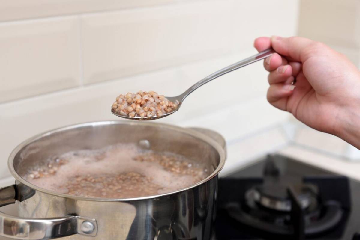 A person scooping cooked lentils from a boiling pot on a stove.