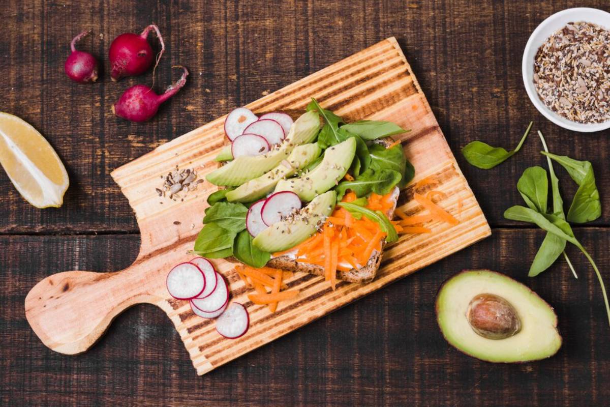 Fresh vegetable toast with avocado, radish, carrot, and spinach on a wooden board on a rustic table.