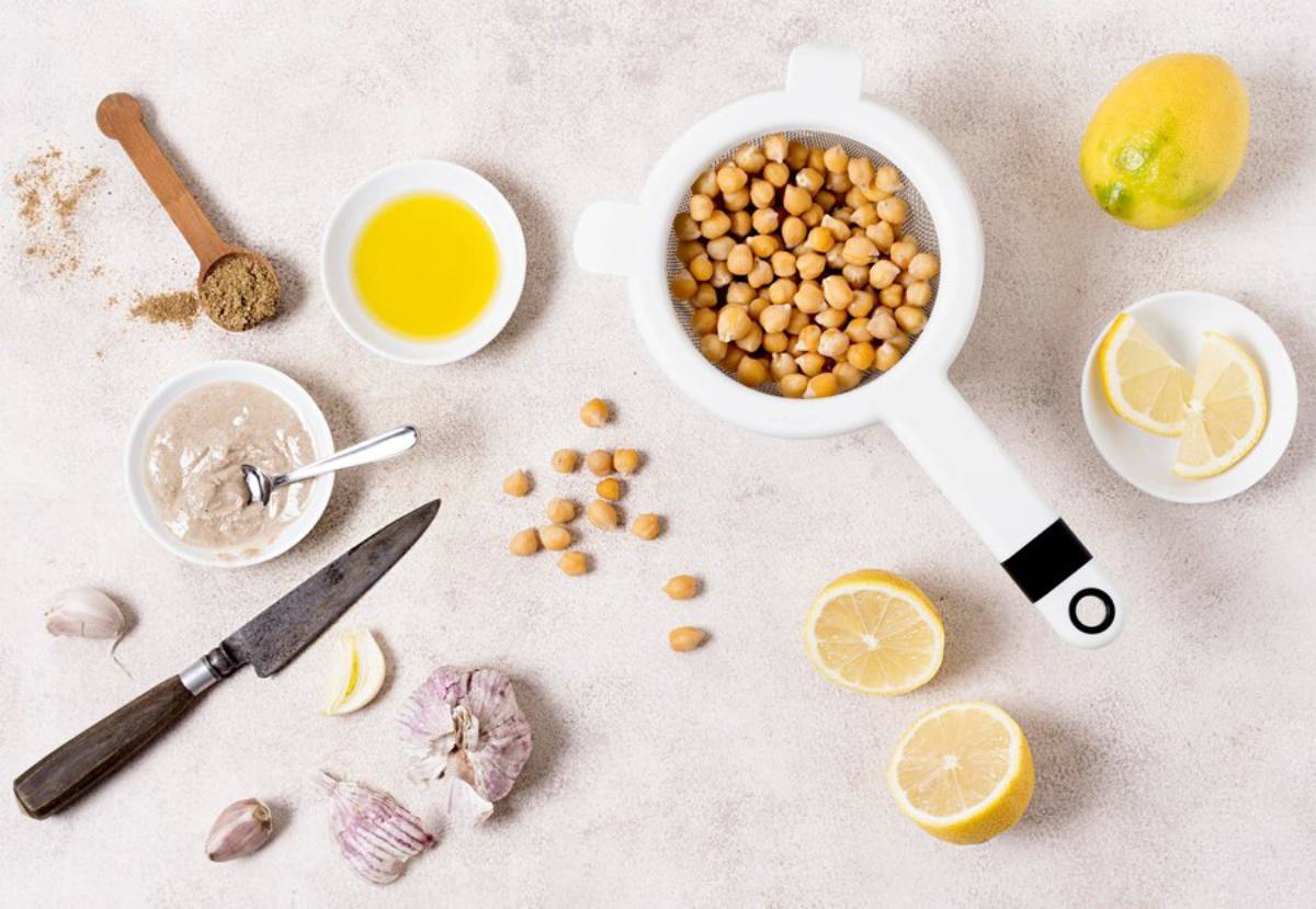 Ingredients for cooking displayed on a countertop, including chickpeas, lemon, garlic, oil, and spices.