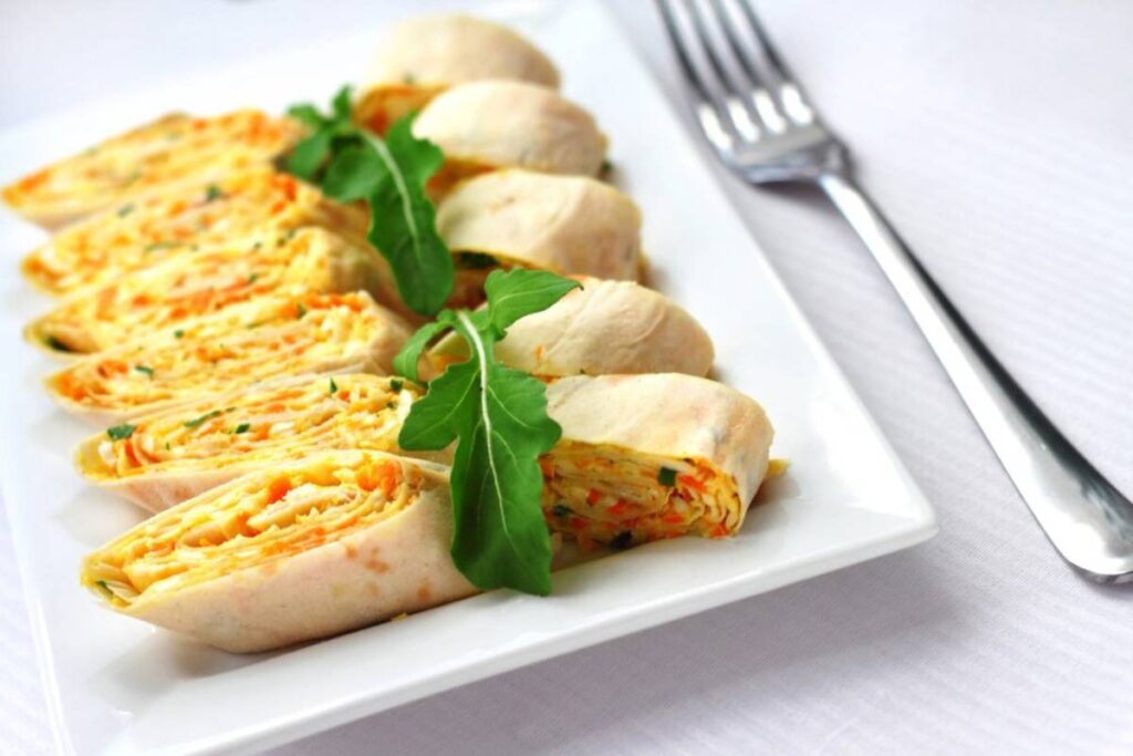 A plate of sliced, stuffed chicken rolls garnished with arugula, served on a white rectangular plate with a fork.