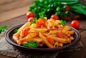 A plate of penne pasta with tomato sauce, cherry tomatoes, and parsley on a wooden table.