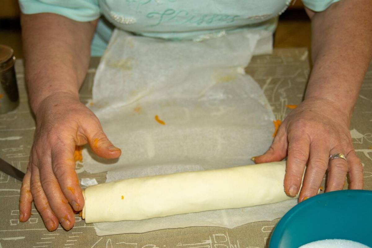 Person rolling dough on a kitchen counter with dusted flour and cooking ingredients visible.