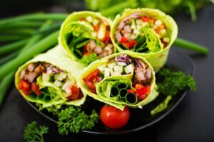 Lettuce wraps containing diced vegetables and meat on a dark plate garnished with fresh herbs.