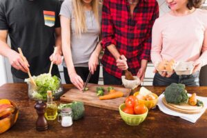 Four people preparing various vegetables and foods on a kitchen counter together.