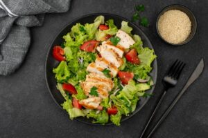 A healthy grilled chicken salad with fresh lettuce, tomatoes, and a side of sesame seeds.