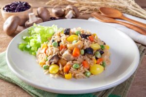 A plate of colorful fried rice with vegetables, cashews, and mushrooms, served on a wooden table.