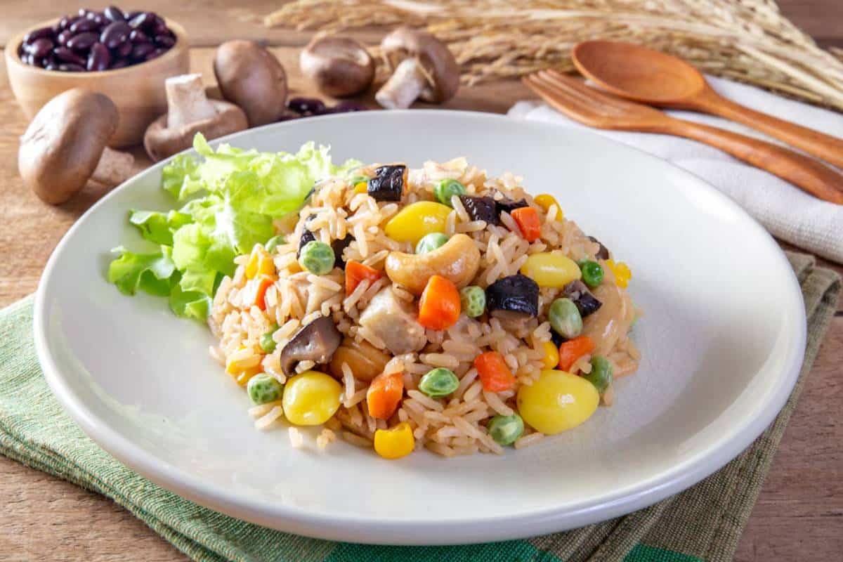 A plate of colorful fried rice with vegetables, cashews, and mushrooms, served on a wooden table.