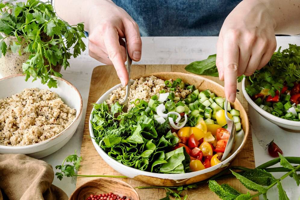 Hands preparing a fresh vegetable salad with quinoa, mixed greens, and colorful chopped vegetables.