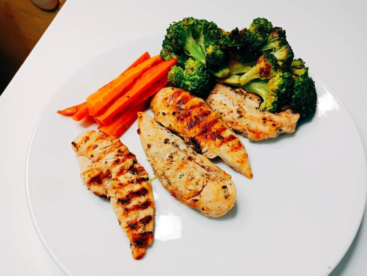 Grilled chicken breasts with steamed broccoli and sliced carrots on a white plate.