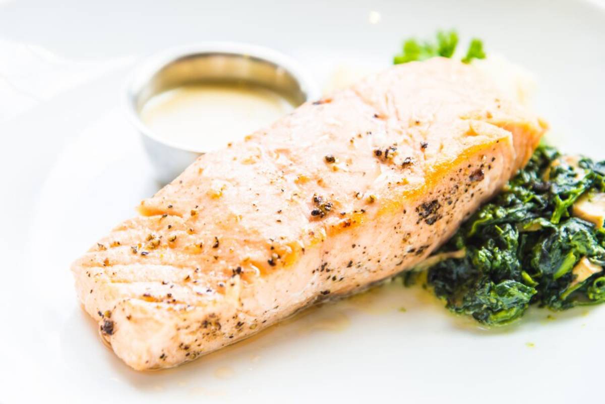 Grilled salmon fillet served with spinach and a side of sauce on a white plate.