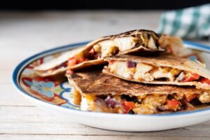 Stacked chicken quesadillas with melted cheese and vegetables on a decorative plate.