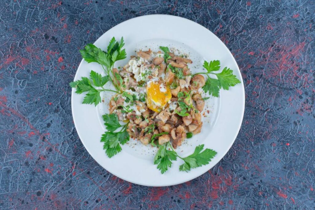A plate of sautéed diced meat with a fried egg, garnished with fresh parsley, served on a marbled blue background.
