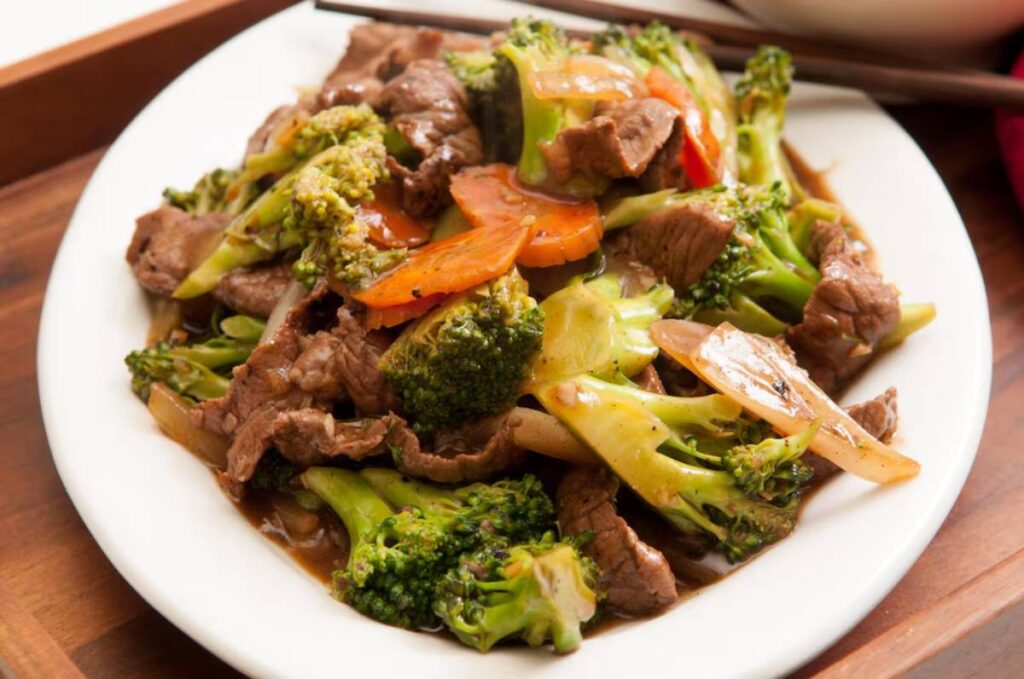A plate of beef stir-fry with broccoli, carrots, and onions, served on a white dish.