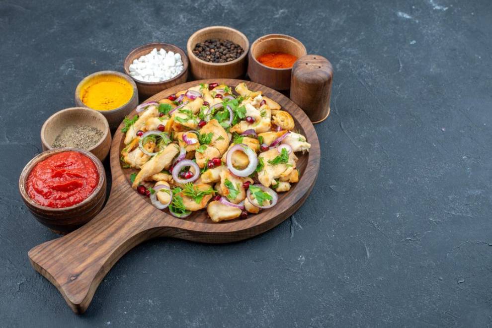 A wooden platter of assorted seafood with garnishes, sauces, and spices on a dark table.