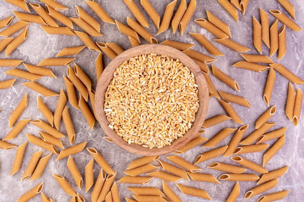 Whole wheat pasta and grains in a wooden bowl on a marble surface.