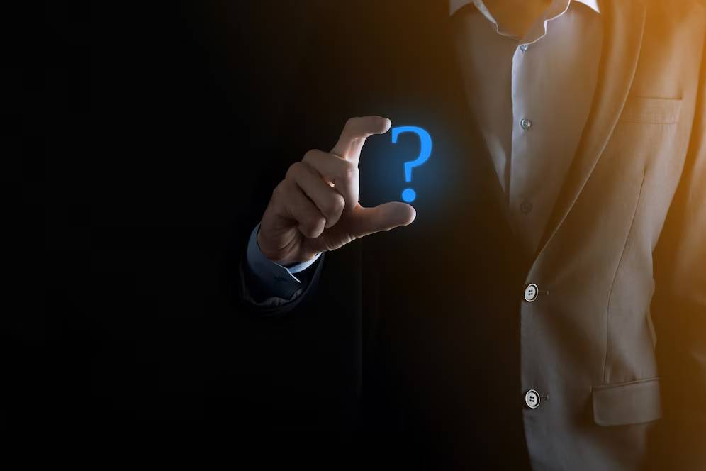 Businessman in dark suit pinching a glowing blue question mark in the air, concept of inquiry or decision-making.