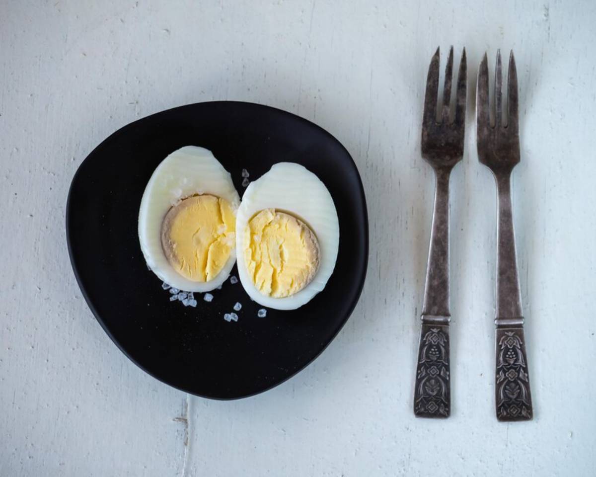 Two perfectly boiled eggs, halved, sit on a black plate with a sprinkle of salt, accompanied by ornate silver forks.