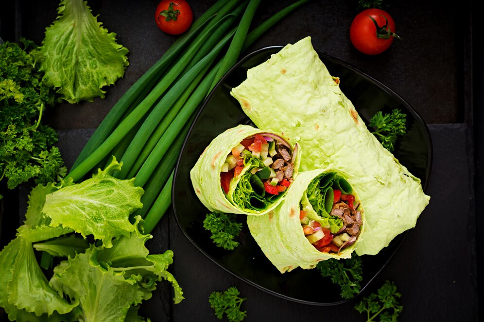 Lettuce wraps filled with colorful vegetables and beef, garnished with fresh greens and tomatoes on a dark plate.