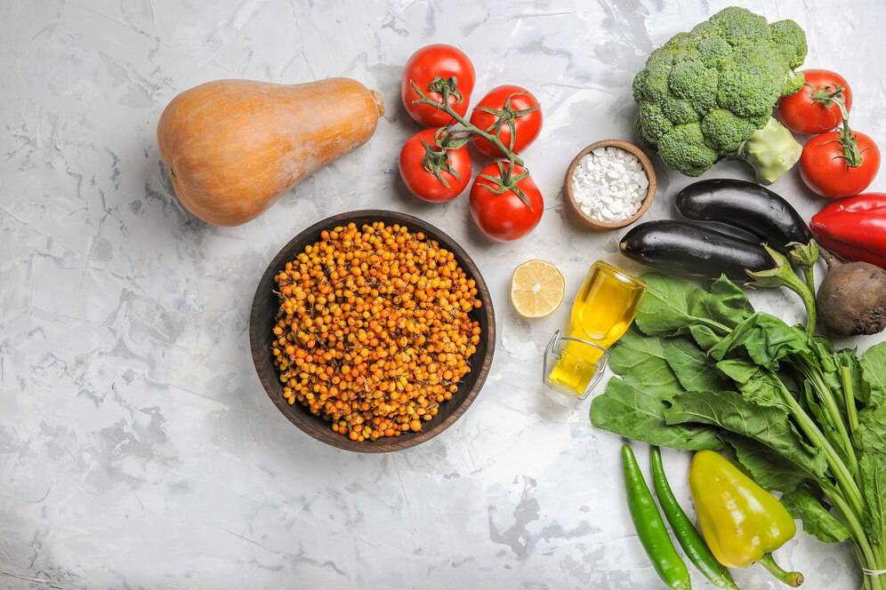 Assorted fresh vegetables and a bowl of cooked lentils arranged neatly on a marble background.