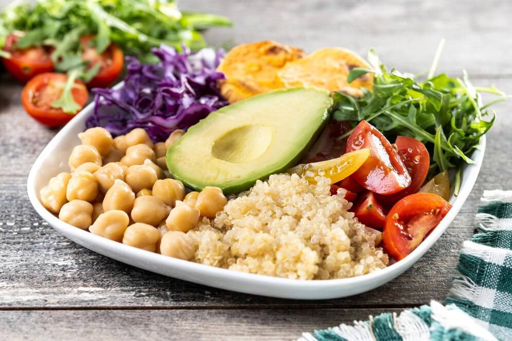A colourful vegan bowl with quinoa, chickpeas, avocado, and mixed vegetables on a wooden table.